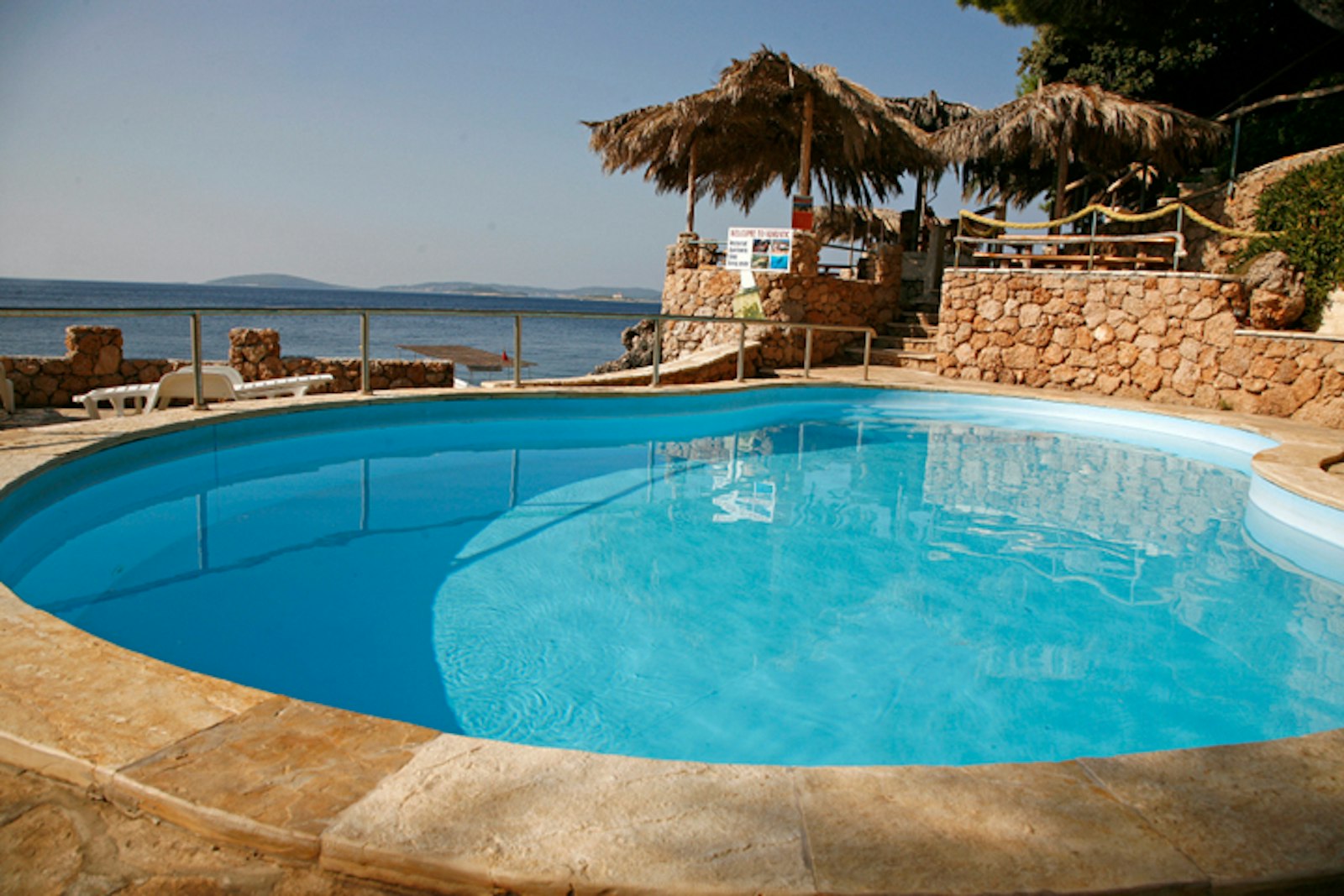Seaside pool right above the Adriatic, straw umbrellas at the bar