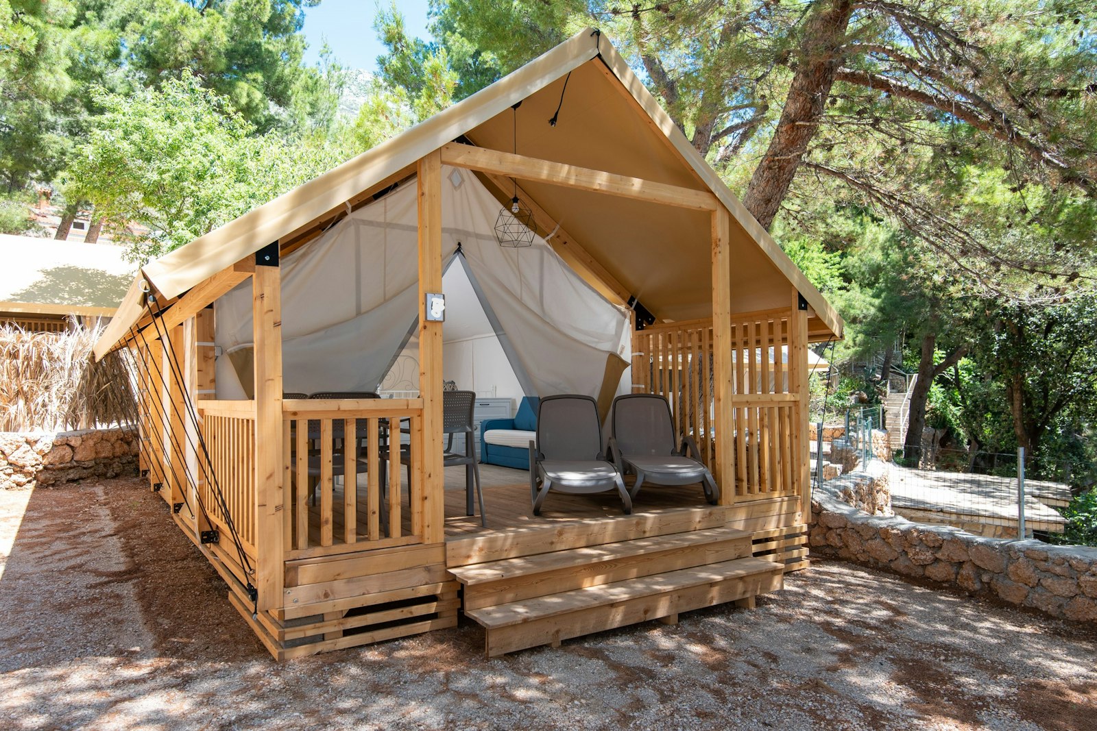 The actual glamping tent under the pines — terrace, loungers, wooden deck